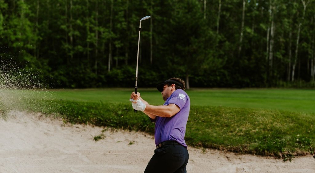 A golfer making a swing in a sand trap