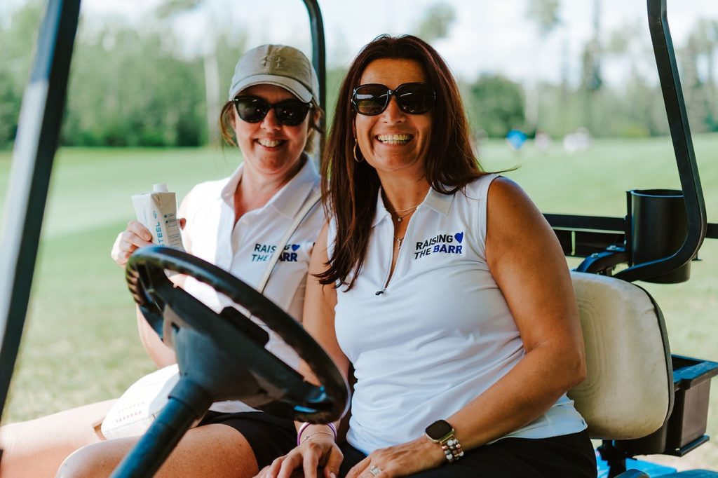 Two smiling women sit in a golf cart